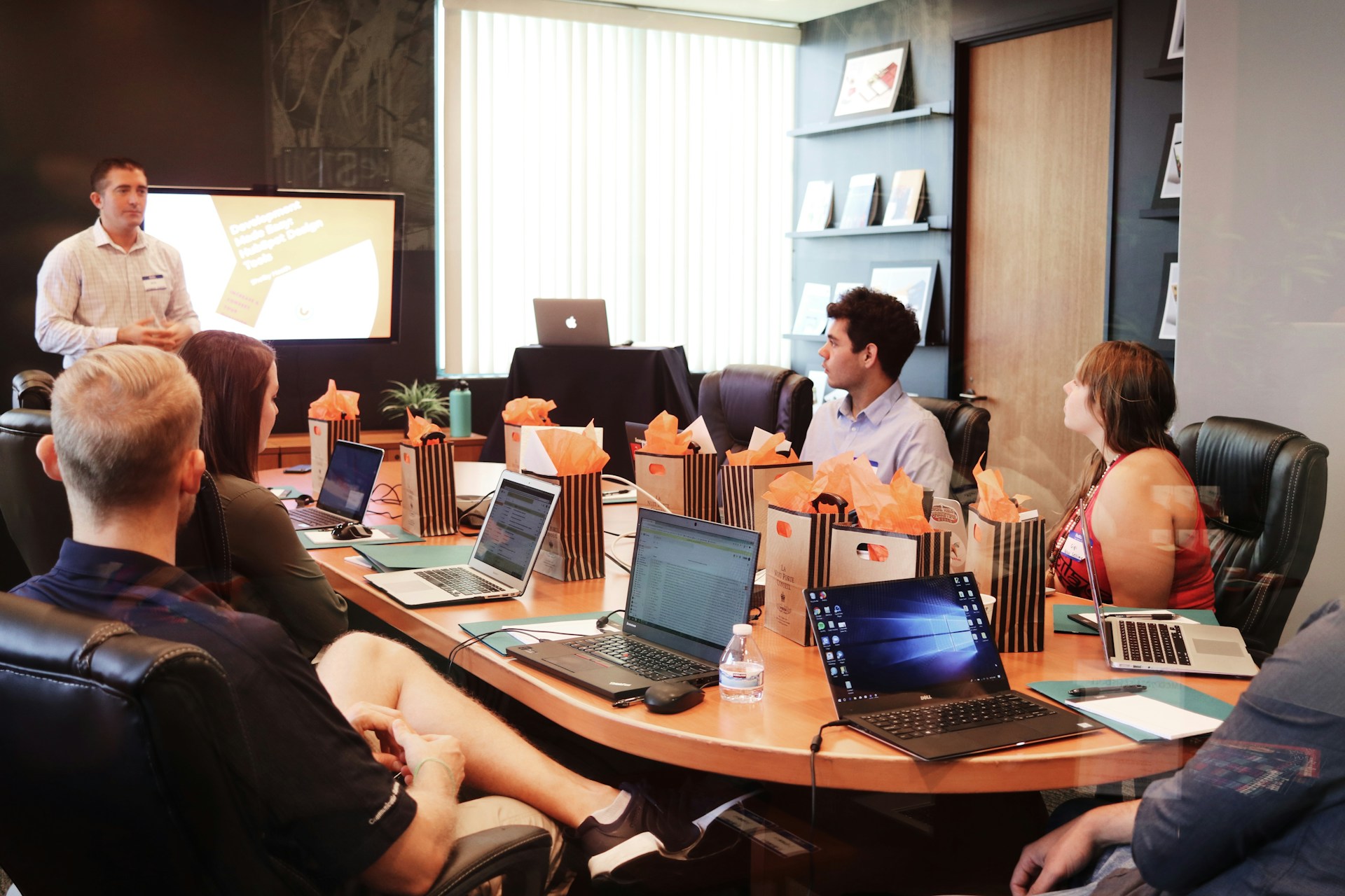 multiple-people-sitting-around-a-desk-listening-to-someone-give-a-business-presentation